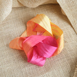 Pink, Orange, and yellow ribbon artistically laying in a twisted fashion on a light brown textured fabric background.