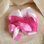 Pink and white ribbon artistically laying in a twisted fashion on a light brown textured fabric background.
