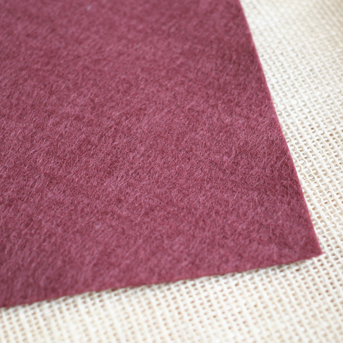 Maroon wool felt sheet with soft textured surface, shown at an angle.