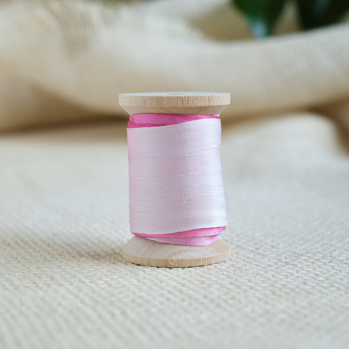 Pink silk ribbon spool on wooden base